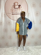 The Alva Boo Dress is all about cozy meets chic! This cotton hoodie dress features a zipper-up front, puff sleeves, and distressed string details for an elevated casual look. Available in a stylish gray, blue, and yellow combo.